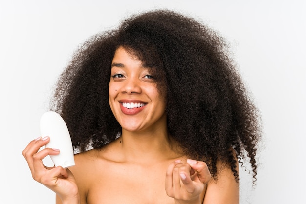 Young afro woman holding a moisturizer isolated pointing with finger at you as if inviting come closer.