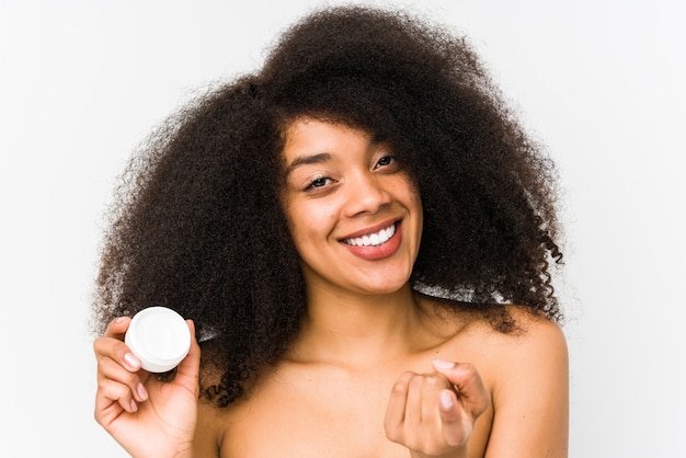 Young afro woman holding a moisturizer isolated pointing with finger at you as if inviting come closer.