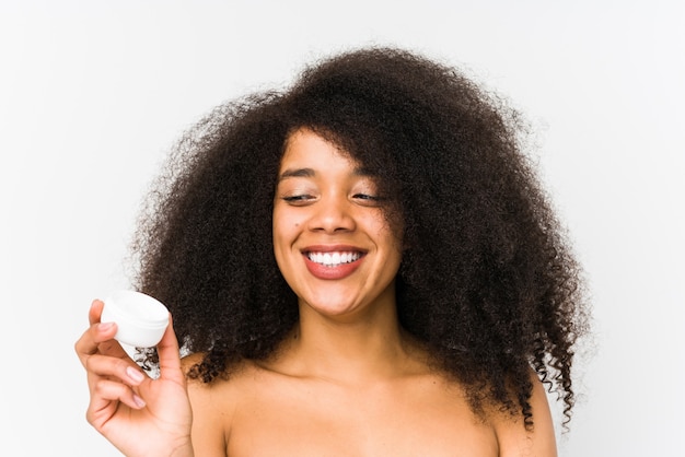 Young afro woman holding a moisturizer smiling confident with crossed arms.