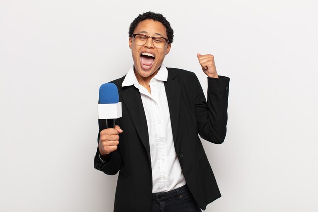 Young afro woman shouting aggressively with an angry expression or with fists clenched celebrating success