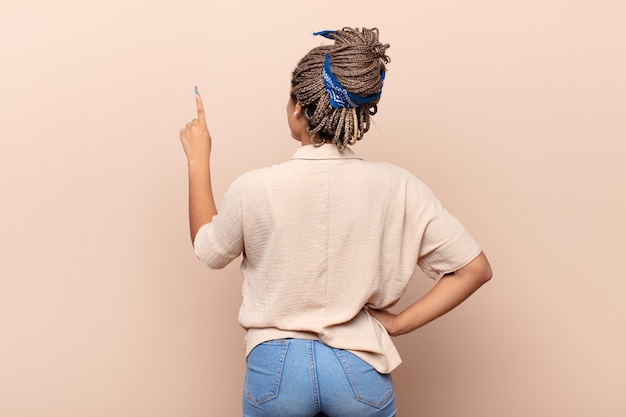 Photo young afro woman standing and pointing to object on copy space, rear view