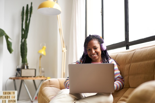 Young afroamerican woman telecommuting from home using a laptop chatting or surfing the internet