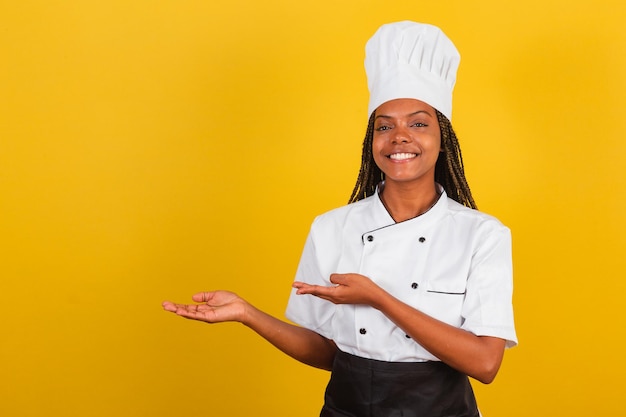 Young afrobrazilian woman chef presenting something to the left pointing at something