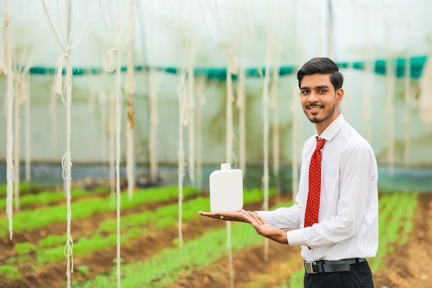 Young agronomist holding bottle in hand at greenhouse