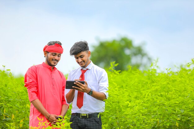 Young agronomist showing some information in tablet to farmer at green field