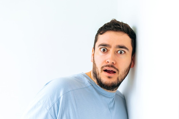 Young amazed bearded man kistening to the gossips through the wall looking at camera