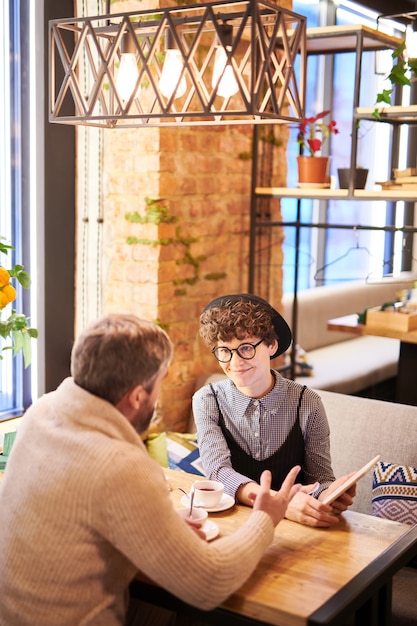 Young amorous couple with touchpad discussing online video while sitting in luxurious cafe or restaurant