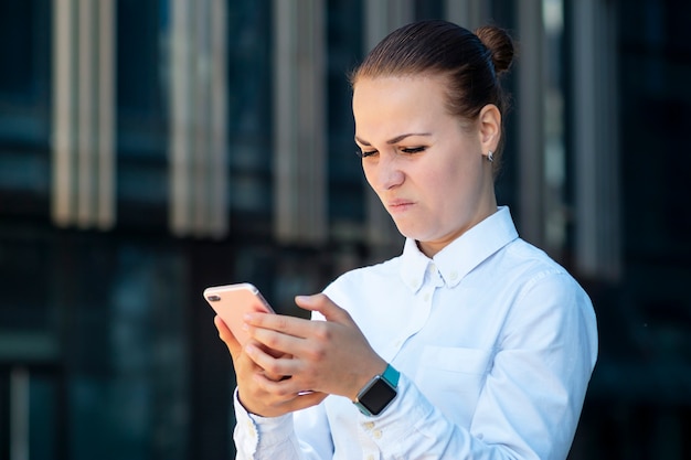 Young angry frowning disgusted business woman surfing smartphone in dislike