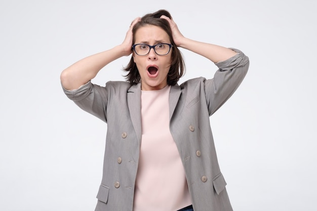 Young angry shocked woman in glasses holding hands on head