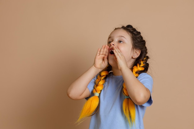 Young anxious girl shouting with opened mouth and holding hands by mouth and asking someone for help having kanekalon braids of yellow color looking up on beige background