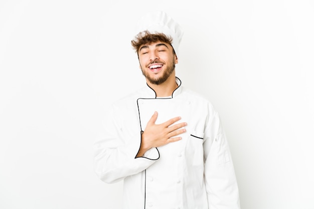 Young arab cook man laughs out loudly keeping hand on chest.