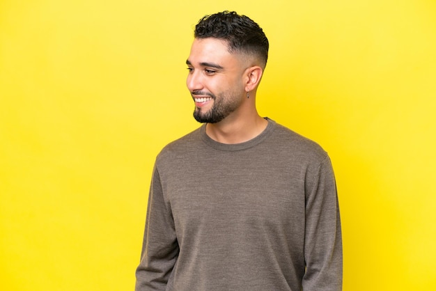 Young Arab handsome man isolated on yellow background looking to the side and smiling