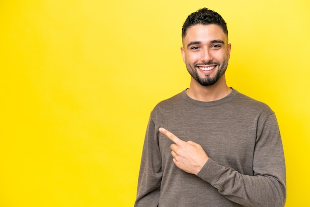 Young Arab handsome man isolated on yellow background pointing to the side to present a product