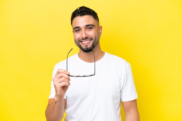 Young Arab handsome man isolated on yellow background With glasses with happy expression