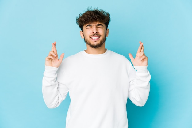 Young arab man on blue wall crossing fingers for having luck