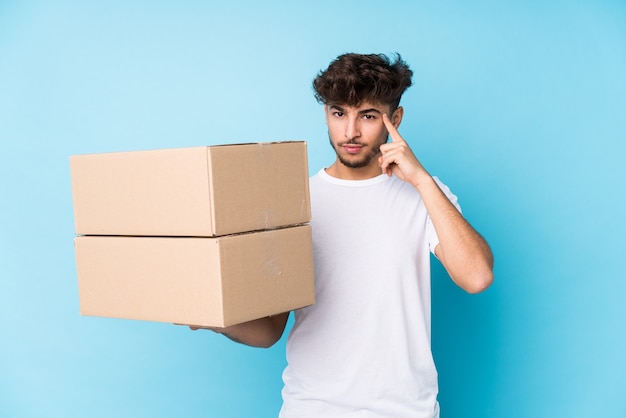 Young arab man holding boxes isolated pointing temple with finger, thinking, focused on a task.