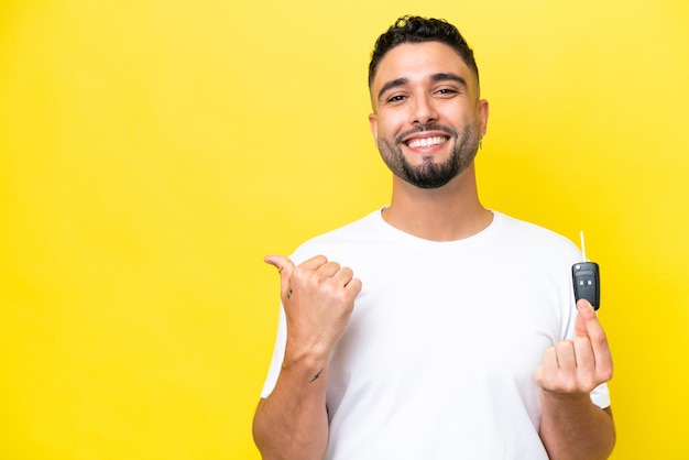 Young Arab man holding car keys isolated on yellow background pointing to the side to present a product