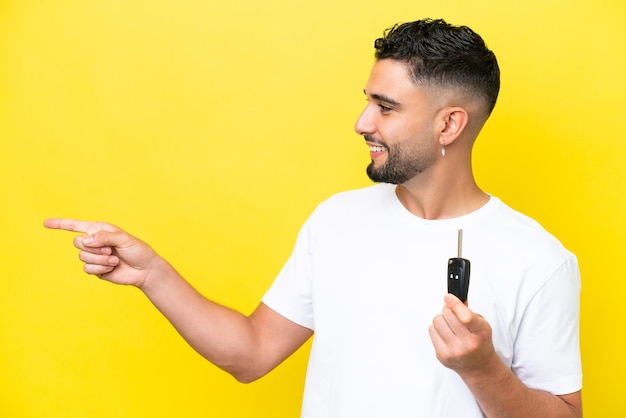 Young Arab man holding car keys isolated on yellow background pointing to the side to present a product