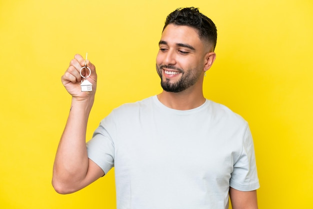 Young Arab man holding home keys isolated on yellow background with happy expression