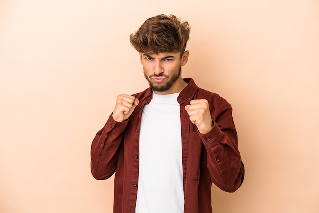 Young arab man isolated on beige background showing fist to camera, aggressive facial expression.