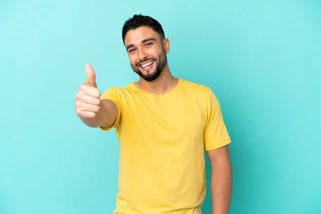 Young arab man isolated on blue background with thumbs up because something good has happened