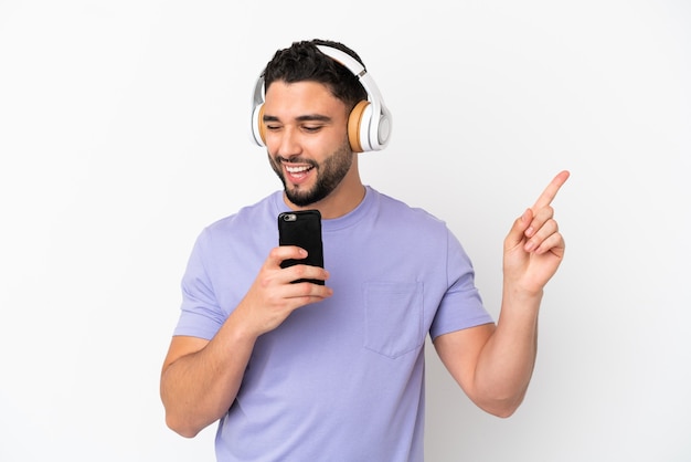 Young arab man isolated on white background listening music with a mobile and singing