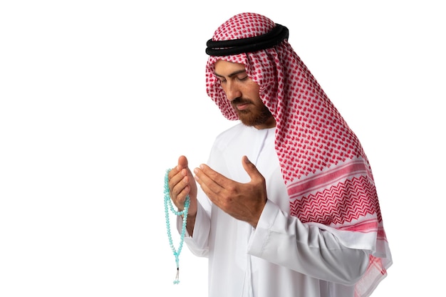 Young Arab man in traditional clothes holding beads isolated on white background