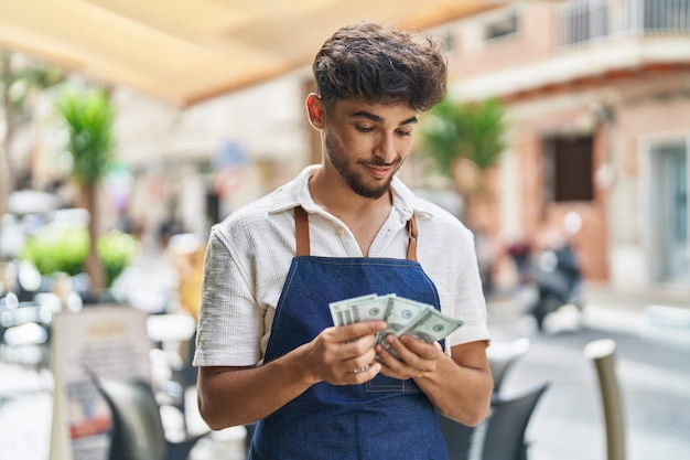 Young arab man waiter counting dollars working at restaurant