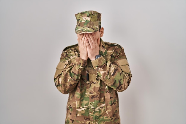 Photo young arab man wearing camouflage army uniform with sad expression covering face with hands while crying. depression concept.