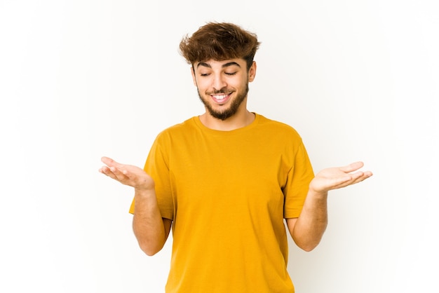 Young arab man on white background holding something with palms, offering to camera.