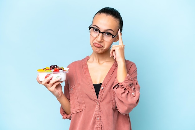 Young Arab woman holding a bowl of fruit isolated on blue background thinking an idea