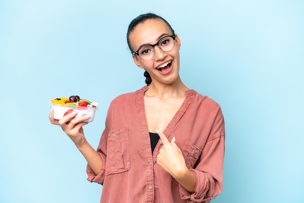 Young Arab woman holding a bowl of fruit isolated on blue background with surprise facial expression