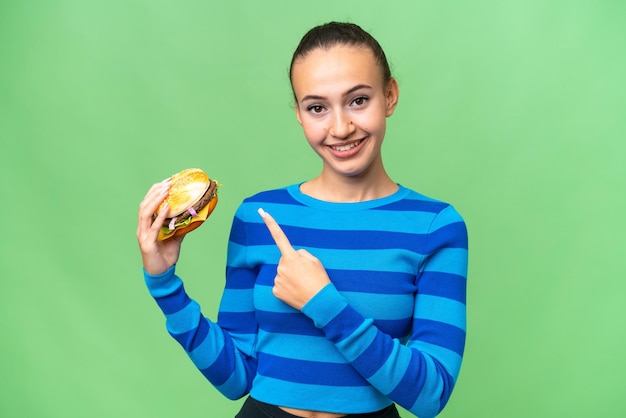 Young Arab woman holding a burger over isolated background pointing to the side to present a product