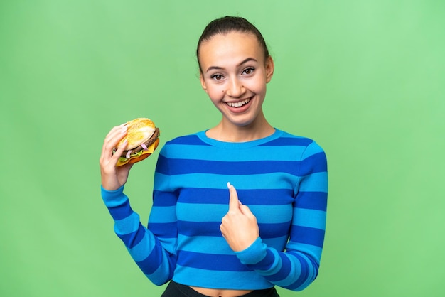 Young Arab woman holding a burger over isolated background with surprise facial expression