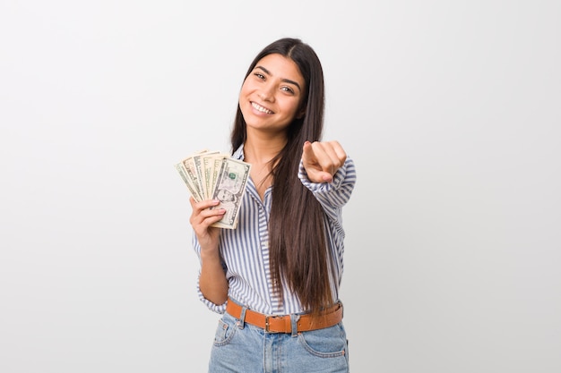 Young arab woman holding dollars cheerful smiles pointing to front.