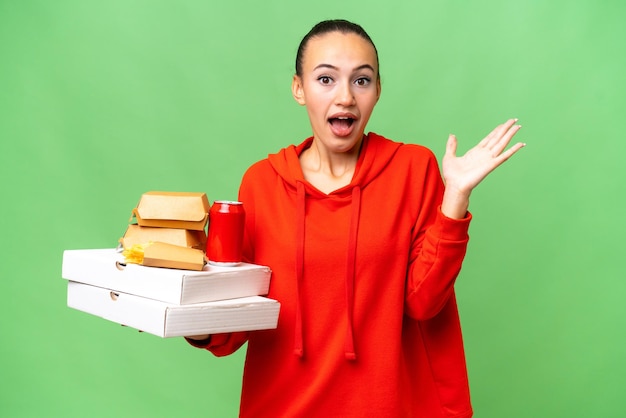 Young Arab woman holding fast food over isolated background with shocked facial expression