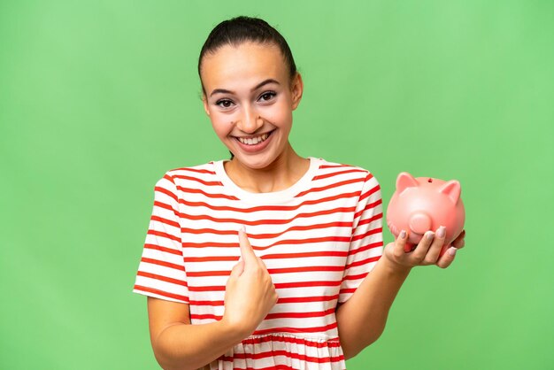 Young Arab woman holding a piggybank over isolated background with surprise facial expression