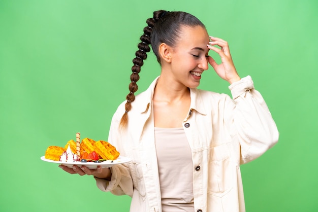 Young Arab woman holding waffles over isolated background laughing