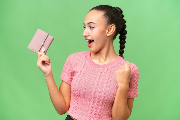 Young Arab woman holding a wallet over isolated background celebrating a victory