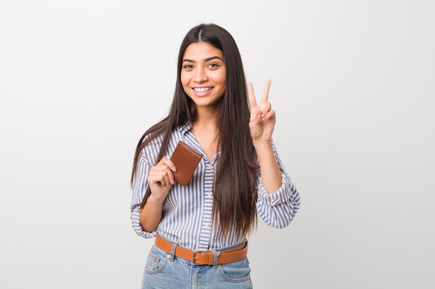 Young arab woman holding a wallet showing victory sign and smiling broadly.