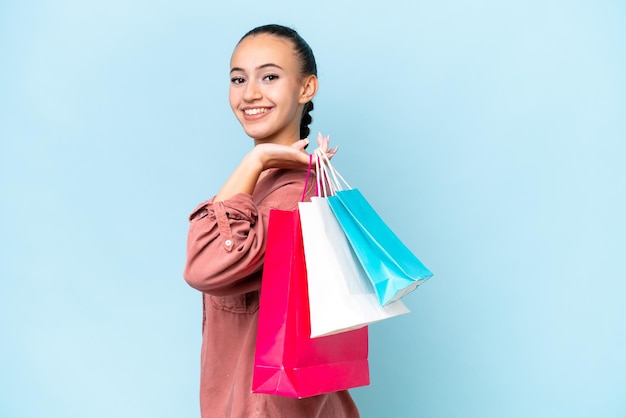 Young Arab woman isolated on blue background holding shopping bags and smiling