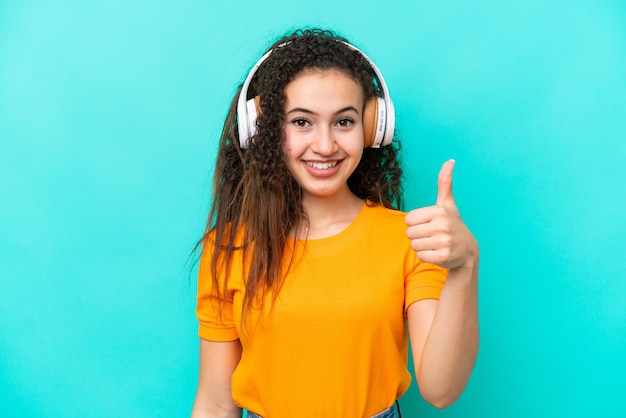 Young Arab woman isolated on blue background listening music and with thumb up