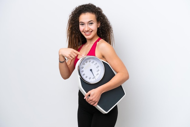 Young Arab woman isolated on white background holding a weighing machine and pointing it