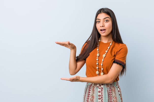 Young arab woman shocked and amazed holding a copy space between hands.