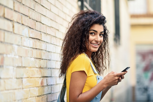 Young Arab woman texting with her smart phone on brick urban wall.