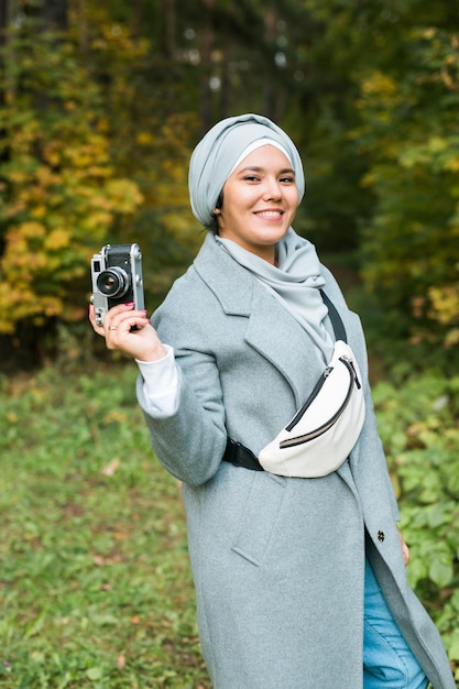 Young Arab Woman wearing hijab headscarf photographing with a smartphone in park. Modern muslim girl.