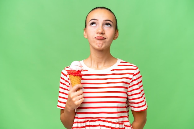 Young Arab woman with a cornet ice cream over isolated background and looking up