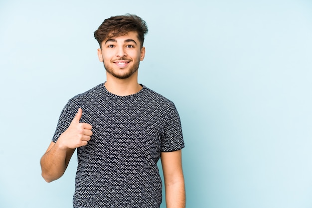 Young arabian man isolated on a blue background smiling and raising thumb up