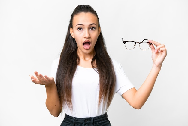 Young Arabian woman holding glasses over isolated white background with shocked facial expression