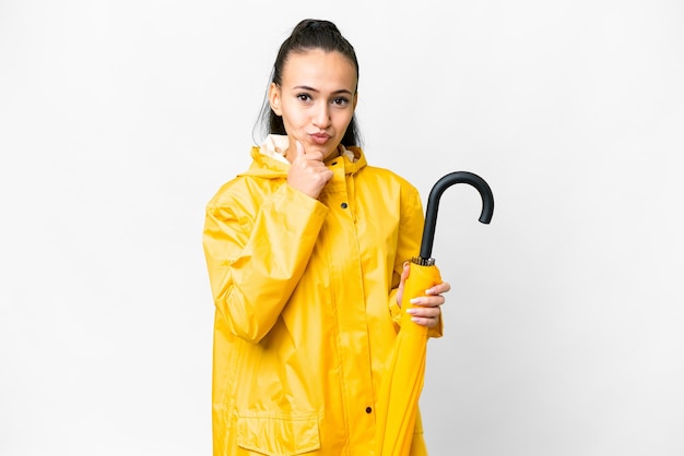 Young Arabian woman with rainproof coat and umbrella over isolated white background thinking